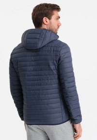 Giacca imbottita blu navy con cappuccio, caratterizzata da dettagli di cuciture orizzontali, chiusura con zip e polsini elastici, progettata per il calore e il comfort.