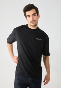 Black cotton t-shirt with short sleeves, crew neck, featuring a small white printed logo on the chest. Smooth texture and relaxed fit.
