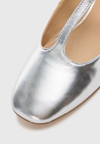 Silver leather shoe featuring a sleek design, open side cutouts, rounded toe, and smooth texture with a subtle sheen.