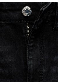 Jeans de mezclilla negra con un botón plateado, cremallera metálica y costuras visibles a lo largo de la pretina y la zona de la bragueta.