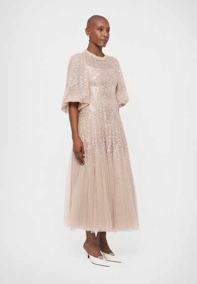 Beżowa sukienka z tiulu z cekinami, krótkimi bufkami i warstwową spódnicą. Połączona z białymi butami na obcasie w szpic z dekoracyjnymi akcentami.