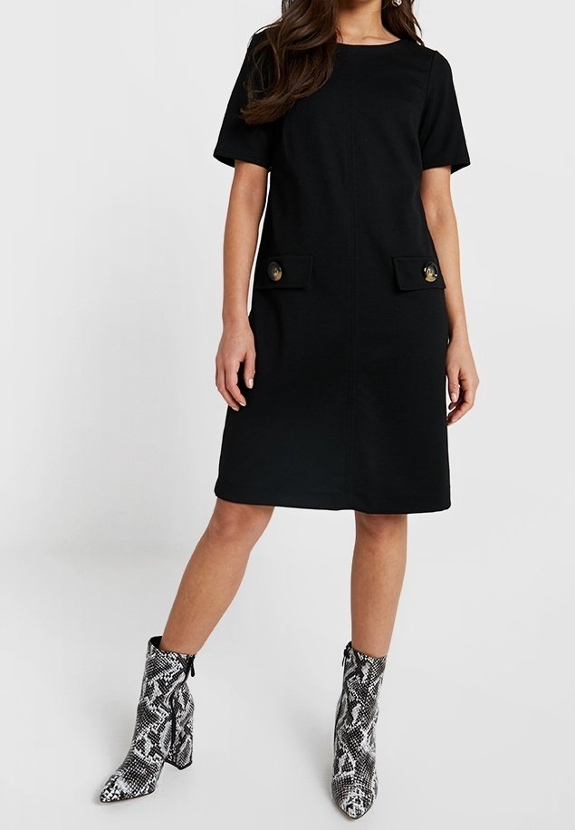 Černé šaty s krátkým rukávem, dvěma předními kapsami a zlatými knoflíkovými detaily. V kompletu s černobílými koženými kotníkovými botami s hadím vzorem. Hladká textura.
