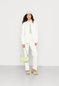 Camisa oversized branca, blusa floral verde, chapéu de balde verde claro, calças de creme e bolsa verde a condizer; sandálias de salto alto completam o look.