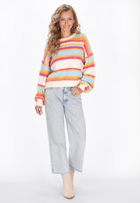 Mehrfarbiger Pullover mit horizontalen Streifen in Pink, Orange, Blau und Creme. Kuscheliger Stoff, runder Ausschnitt und Ballonärmel, kombiniert mit hellen Jeans.