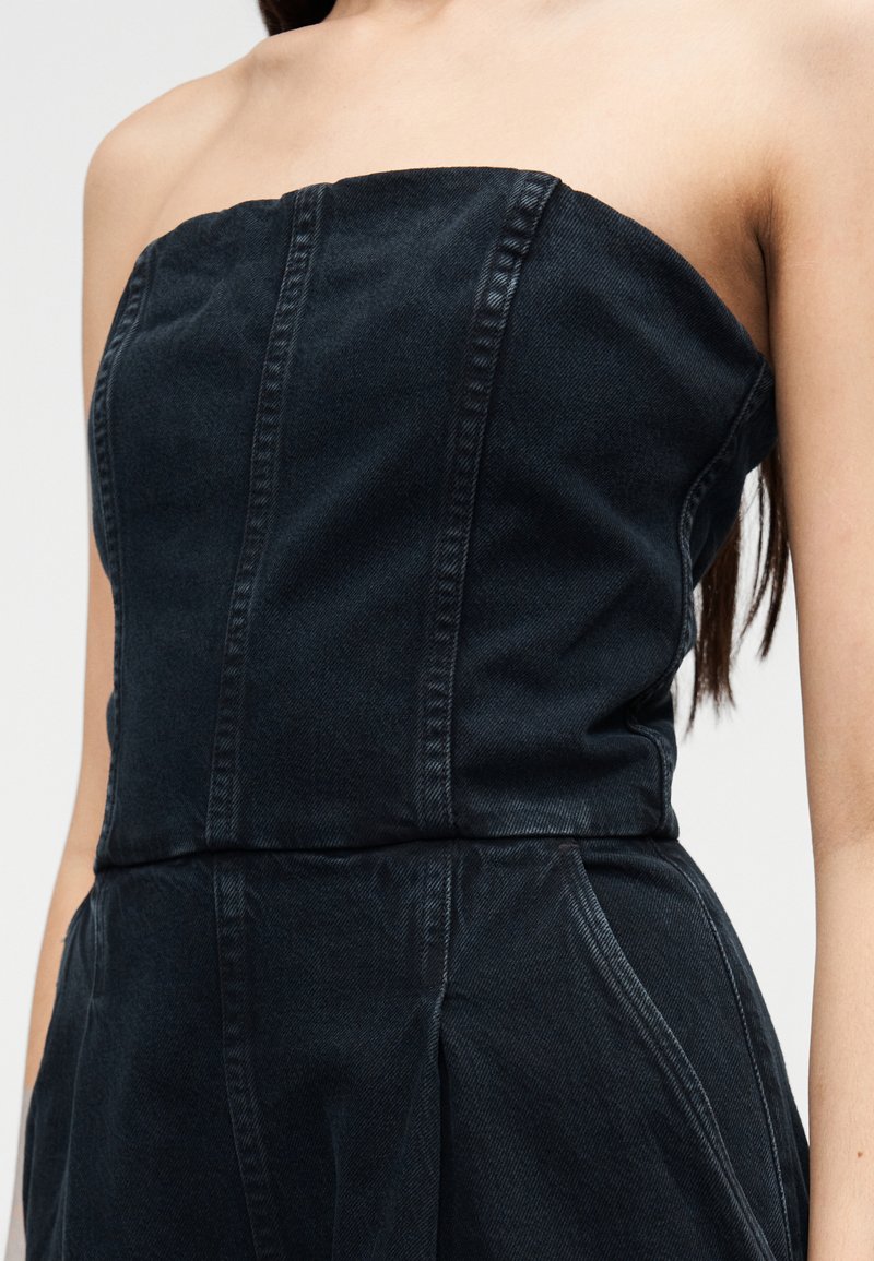 Haut bustier en denim foncé avec des coutures verticales, un design structuré et un léger éclat. Le tissu est lisse avec une silhouette ajustée.