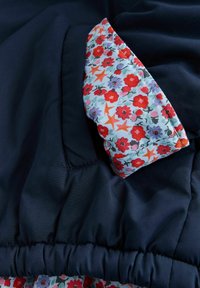 Jachetă albastru închis cu căptușeală interioară florală albastru deschis, cu flori roșii și stele portocalii. Tiv elastic și textură fină.