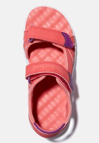 Korallrosa sandal med två justerbara kardborreband och en strukturerad innersula. Har en lila accent på bandet och vit sula.
