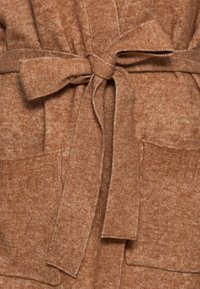 Hnědý pletený župan s měkkou texturou, s vázáním a dvěma předními kapsami. Tkanina má jemný melírovaný vzor.