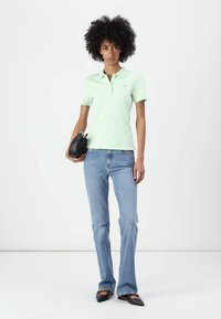Lys grøn polo-skjorte med krave; parret med lys blå flagrende jeans. Holder en liten svart veske; svarte spissede sko.
