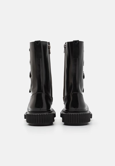 Black patent leather ankle boots with a chunky rubber sole, featuring a side zipper and decorative hardware details.