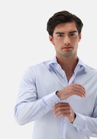 Hellblaues Hemd aus glattem Stoff, mit spitzem Kragen, knöpfbaren Manschetten und einem schlanken Schnitt.