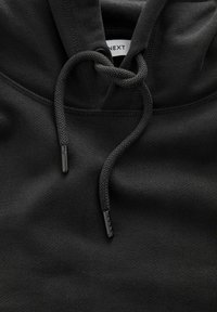 Gros plan sur le tissu d'un sweat à capuche noir montrant des cordons torsadés et une étiquette de marque blanche à l'intérieur du col.