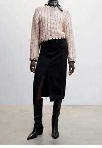 Maglione lavorato a maglia rosa chiaro con un design cropped, abbinato a una gonna di jeans nera con uno spacco frontale e stivali neri alti fino al ginocchio con tacco.