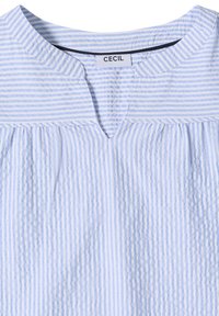 Blouse à rayures verticales bleu clair et blanc avec un col rond présentant une petite découpe en V et un tissu froncé sous la partie supérieure.