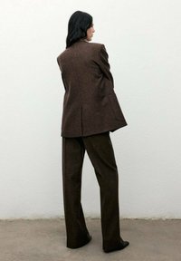 Completo in lana marrone con blazer strutturato e pantaloni a gamba larga, caratterizzato da un tessuto testurizzato e un design liscio e minimalista.