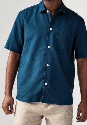 Chemise à manches courtes, boutonnée, en tissu teal profond. Comprend une poche poitrine, des boutons blancs et une coupe décontractée avec une texture lisse.