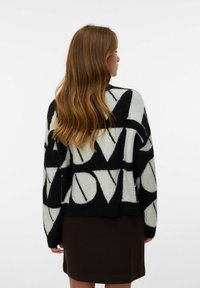 Maglione lavorato a maglia in bianco e nero con grande motivo "LOVE", vestibilità oversize e maniche lunghe; indossato sopra una gonna marrone. Tessuto morbido, design casual.