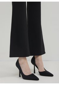 Escarpins noirs à talons hauts avec un bout pointu et une finition satinée. Le design présente une silhouette élégante et un talon aiguille étroit.