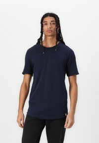 Navy-blaues T-Shirt mit kurzen Ärmeln, runder Ausschnitt, lockere Passform, aus weichem Baumwollmaterial, mit ausgefransten Ärmelkanten und einem kleinen Etikettendetail am Saum.