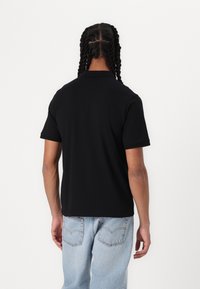 Svart kortermet polo skjorte med krage, glatt tekstur og avslappet passform, kombinert med lyse jeans. Enkel design, ingen synlige mønstre.