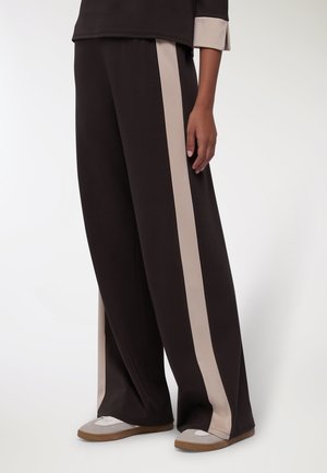 Pantaloni neri a gamba larga con strisce laterali beige, realizzati in un tessuto morbido. Abbinati a scarpe grigie chiare e beige, con un design casual.