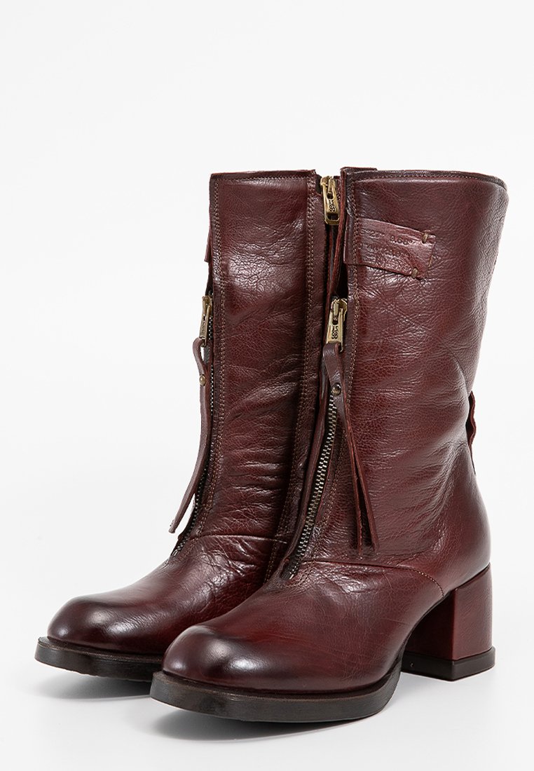 Par de botas de cuero marrón oscuro a media pantorrilla con cremalleras frontales y tacones cuadrados, mostrando ligeras arrugas y una punta redondeada suave.