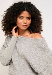Hellgrauer Strickpullover mit strukturiertem Wellenmuster und schulterfreiem Design. Lange Ärmel haben gerippte Bündchen für zusätzlichen Detailreichtum.