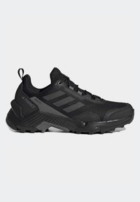 Chaussure de trail running Adidas Terrex noire avec semelle robuste, empeigne en mesh, design à lacets et accents de marque au talon et sur le côté.