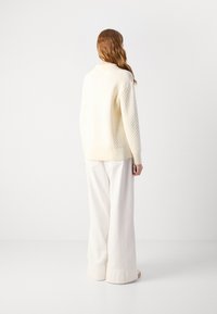 Maglione spesso in crema con motivo testurizzato, maniche larghe e orlo a coste, abbinato a pantaloni bianchi larghi. Finitura complessiva liscia.