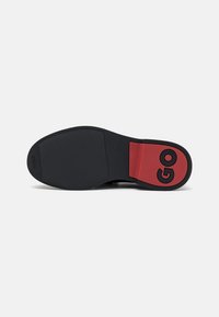 Semelle de chaussure avec une surface en caoutchouc noire, texturée pour l'adhérence, comportant une section rouge marquée du mot "GO" en lettres noires en gras.