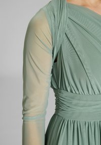 Haalihihja pitkähihainen vaaleanvihreä verkko, jossa on koottu ja poimutettu rintakehä sekä leveä vyötäröosa.