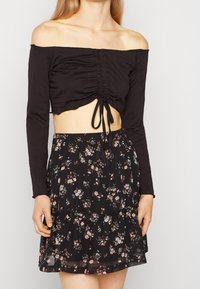 Donna con un top corto nero a spalle scoperte e una mini gonna nera a fiori con piccoli motivi di fiori rosa e bianchi.