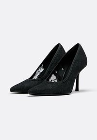 Črne visoke pete z ostrim nosom, ki imajo čipkast prekriv s stranskimi izrezi, z ozko postavitvijo.