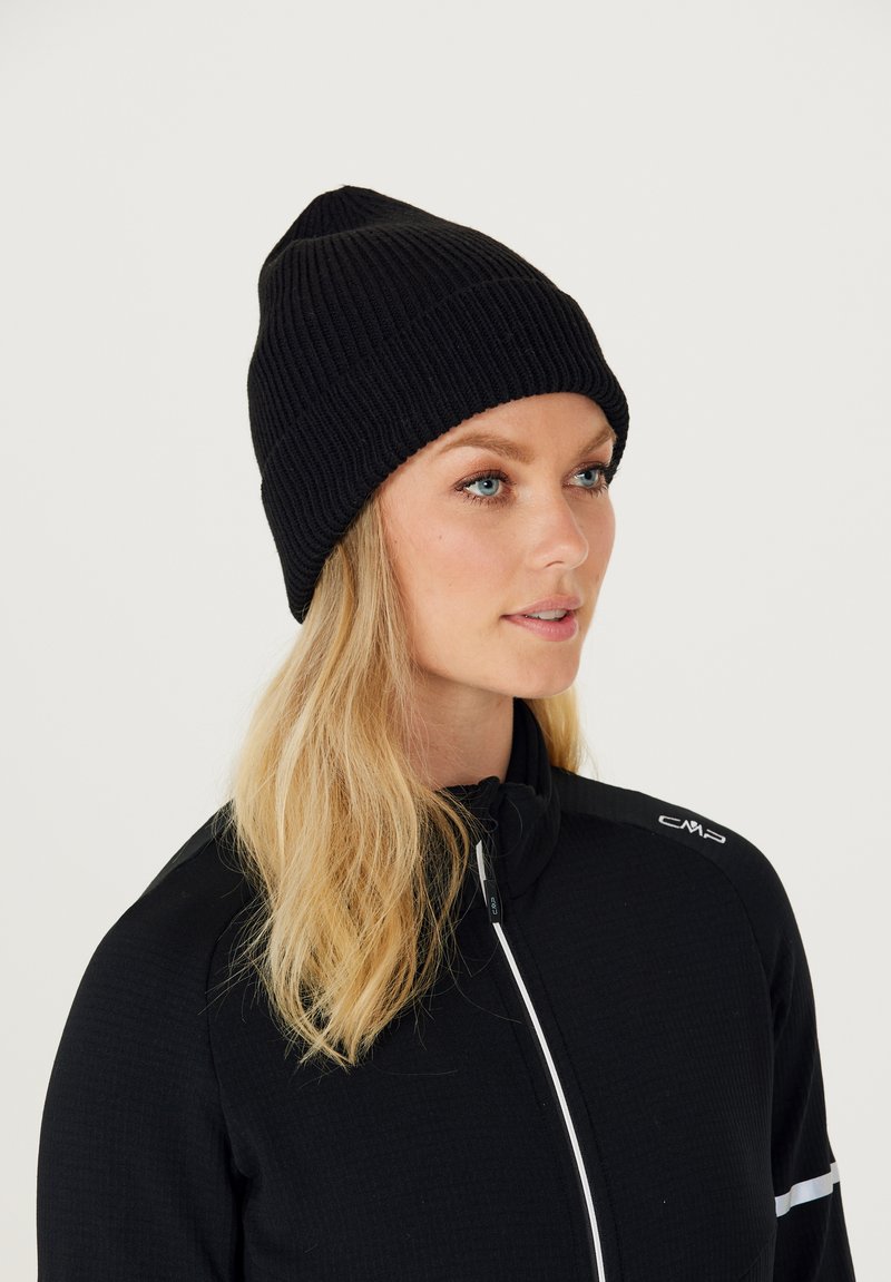 Sort strikket hue med ribbet tekstur og spidst top, båret af en person i en sort zip-up jakke med hvide detaljer.