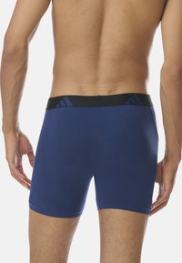 Mörkblå tygboxershorts med ett elastiskt svart midjeband som har tre vertikala ränder. Slät yta och figurnära design.