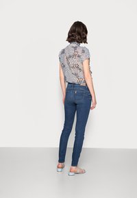 Blusa de manga corta, ligera, con un estampado de leopardo multicolor, combinada con unos vaqueros oscuros ajustados y sandalias de color azul claro.