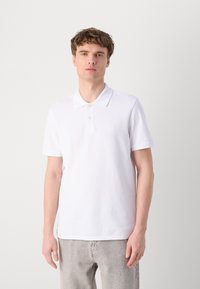 White polo shirt featuring a classic collar, short sleeves, and two button placket. Subtle embroidered logo on the chest. Casual fit.