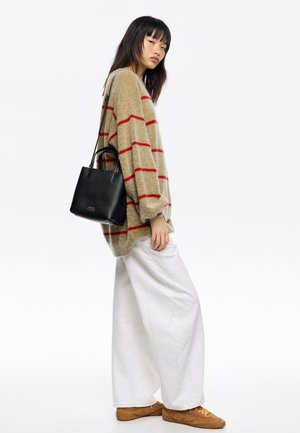 Przeskalowany beżowy sweter z czerwonymi paskami, białe szerokie spodnie i brązowe buty. Czarna teksturowana torba na ramię z uchwytami. Prosty, czysty design.