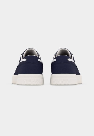 Ζευγάρι μπλε ναυτικό αθλητικά παπούτσια με λευκές σόλες και λευκά κορδόνια, εμφανιζόμενα από πίσω πάνω σε απλό γκρι φόντο.