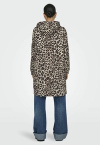 Cappotto con stampa leopardata, in tessuto leggero, di lunghezza media, con maniche lunghe. Abbinato a jeans in denim a gamba larga con orli arrotolati.