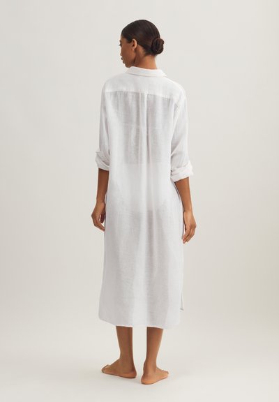 Λευκό φόρεμα πουκάμισο από λινό με ρεβέρ μανίκια, διαθέτει πίσω πιέτα και πλαϊνές σχισμές, φτάνει κάτω από το γόνατο, παρουσιάζοντας ελαφρύ ύφασμα.