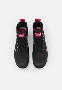 Sneakers alte in tela nera con punte in gomma, con accenti e lacci rossi, marchiati "PALLADIUM" sulla linguetta e sulle linguette del tallone.