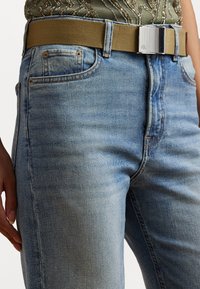 Šviesiai mėlynos džinsinės kelnės su klasikinio kirpimo, penkiomis kišenėmis ir šviesiai ruda elastinga juosta su metaliniu sagtimi ir logotipo detale.