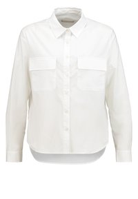 Chemise blanche à manches longues avec col pointu, deux poches poitrine à rabats, coupe ample et ourlet arrondi.
