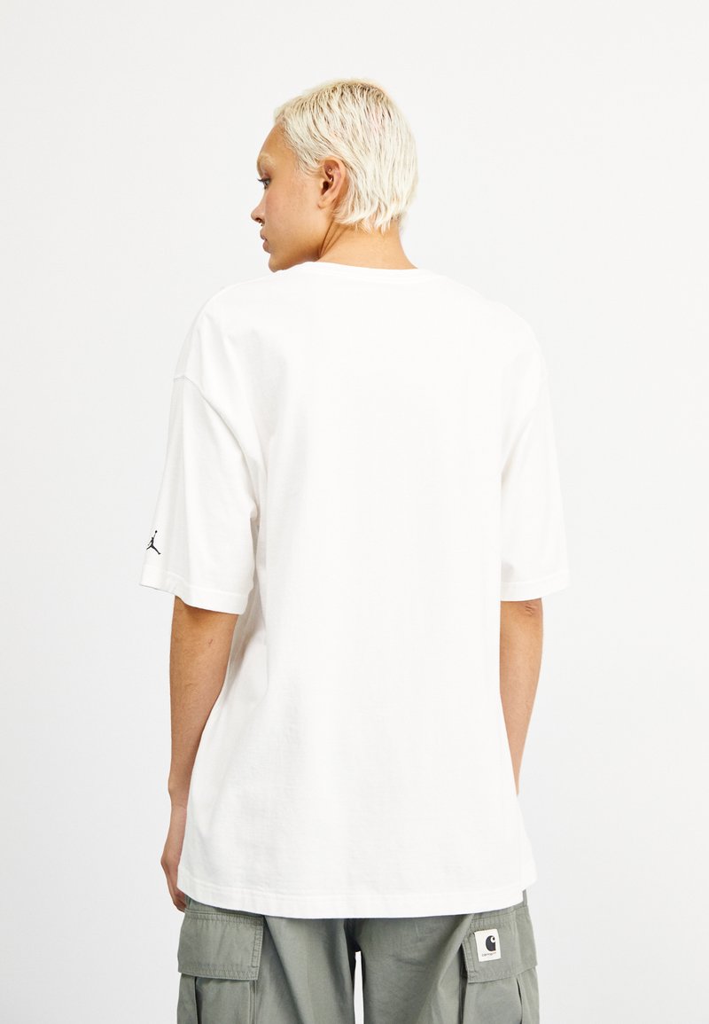  camiseta de algodón blanca de manga corta, corte holgado, con un logo negro de Jordan en la manga izquierda, que muestra una textura suave.