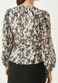 Lang mouwen blouse in doorschijnende, gestructureerde stof met een mix van zwarte, crèmekleurige en gouden tinten; taille met een strik en gathered schouders.