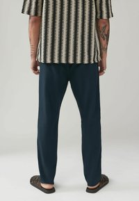 Cămașă cu mânecă scurtă, cu un model alb-negru, pantaloni bleumarin și sandale închise. Cămașa are dungi verticale și un material texturat.
