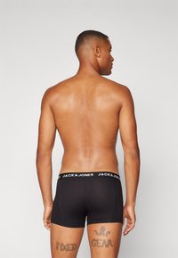 Schwarze Baumwollboxershorts mit einem weißen Bündchen, auf dem das Logo "JACK & JONES" zu sehen ist. Das Modell wird von hinten gezeigt und hat Tattoos.