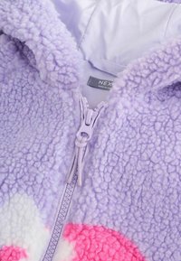Hanorac cu fermoar din fleece violet, cu o suprafață texturată, având modele circulare roz și alb. Include un fermoar de un violet deschis.