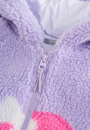 Lilla fleece zip-up hoodie med tekstureret overflade, der har pink og hvide cirkulære mønstre. Inkluderer en lyseblå lynlås.